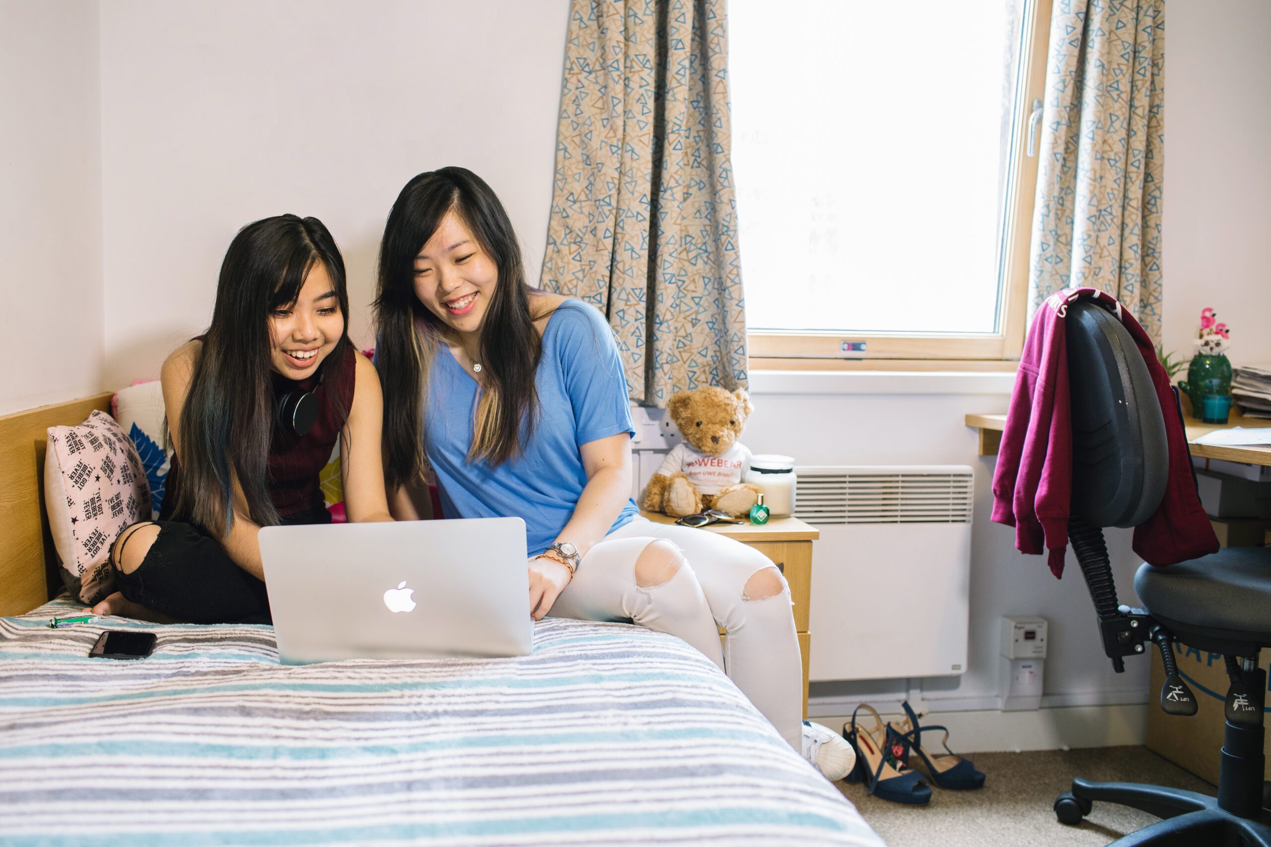Two students sitting on a bed looking at a laptop