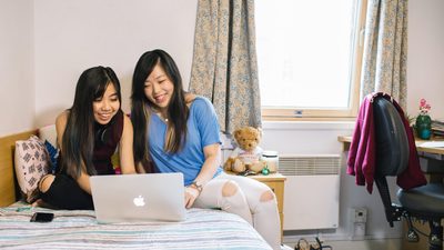 Two students sitting on a bed looking at a laptop