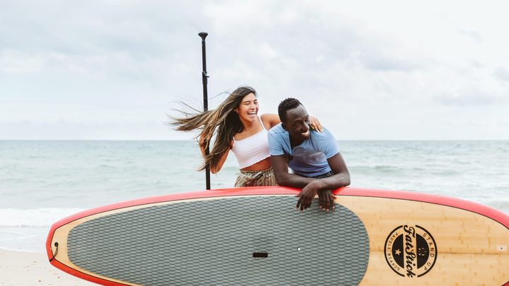 Two people laughing on the beach with a surfboard