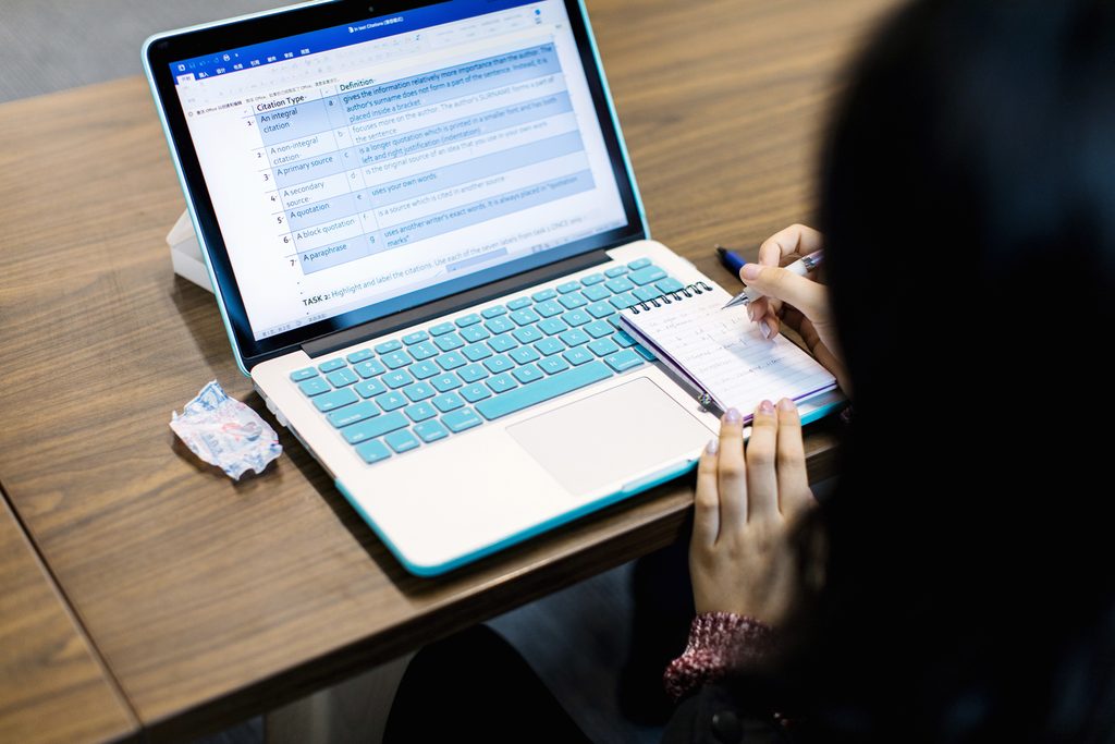 A student taking notes on a pad in front of her laptop