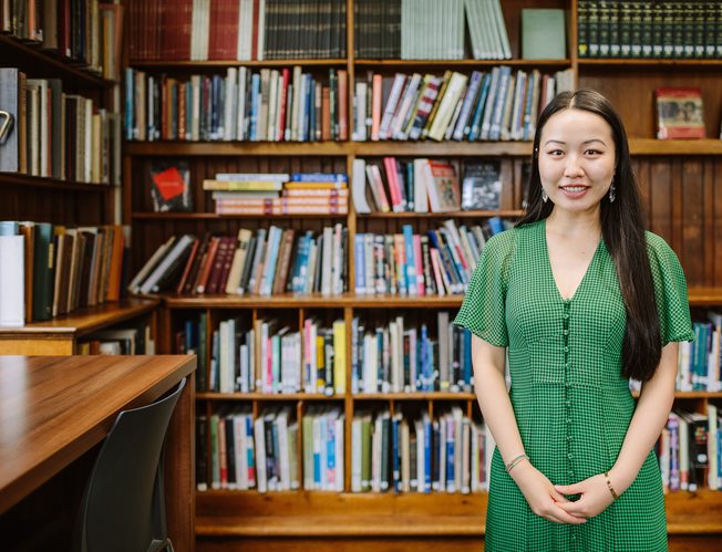 Student Carrie in a library with bookshelves behind her