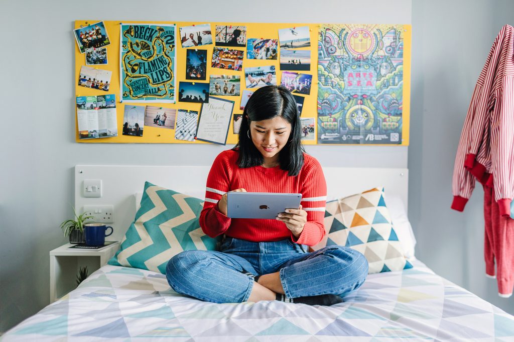 Student sat on the bed and using a tablet in the accommodation