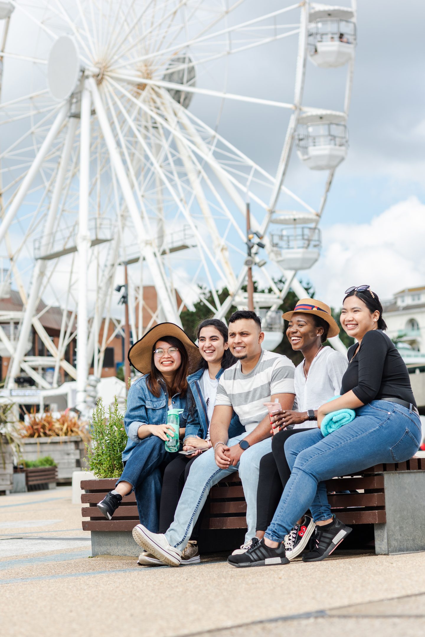 A group of five students on a bench with a ferris-wheel in the background