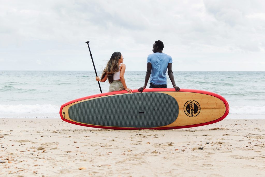 Two students at the beach talking and holding together a stand up paddle board