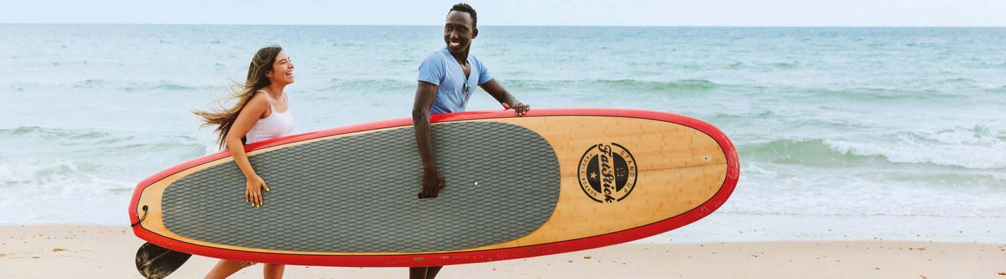 Two students walking on the beach carrying a stand paddle board