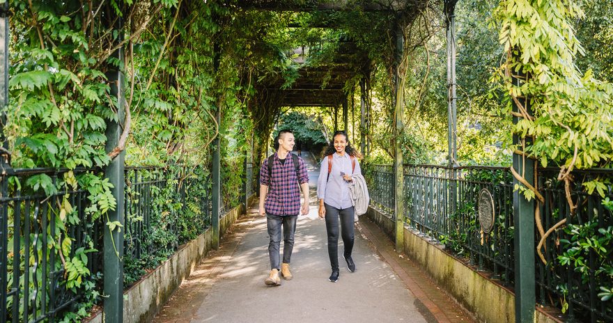 Two students walking through a leafy tunnel