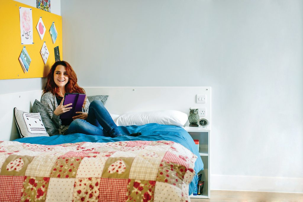 Student sitting on the bed and holding a tablet in the student accommodation