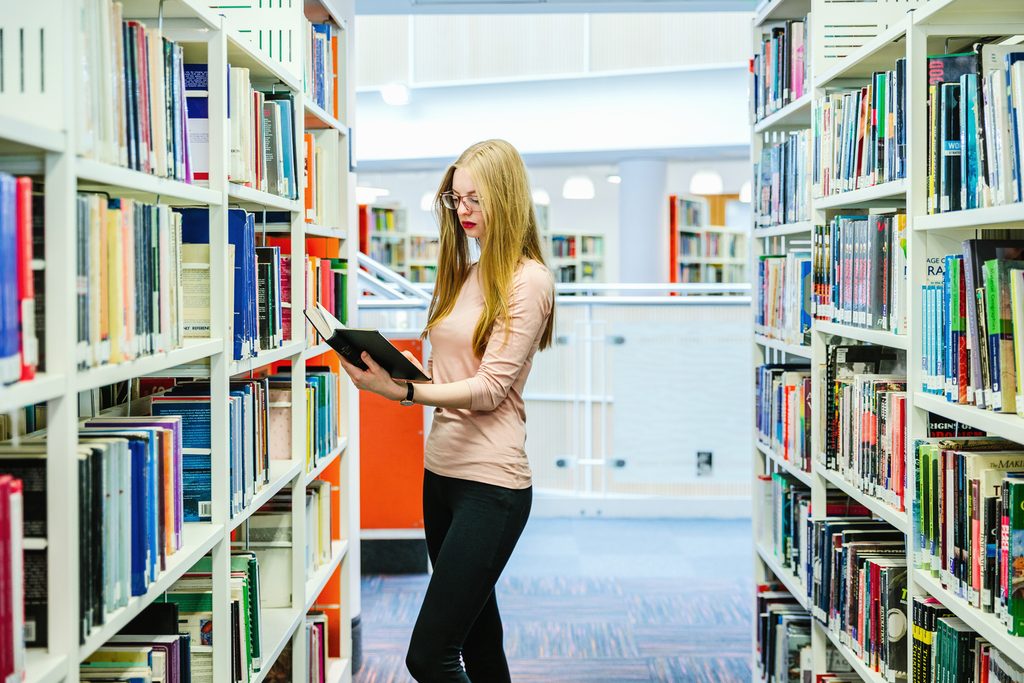 A NTIC student consulting a book in the library