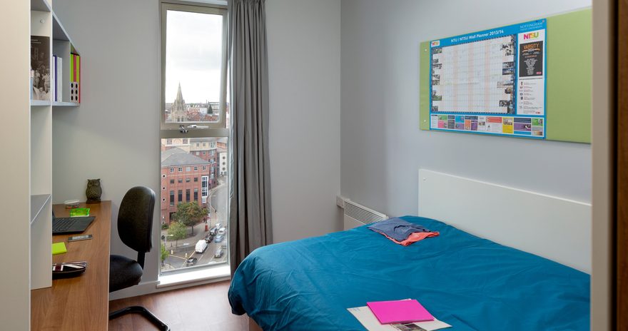 Student bedroom with a city view containing a bed, desk and a chair