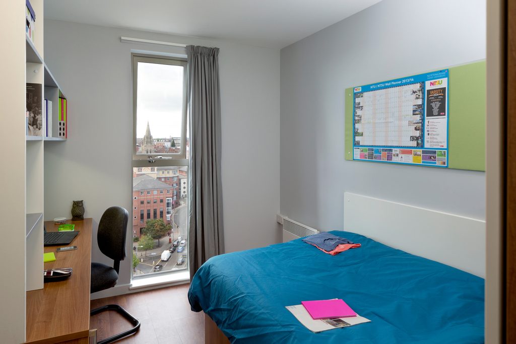 Student bedroom with a city view containing a bed, desk and a chair