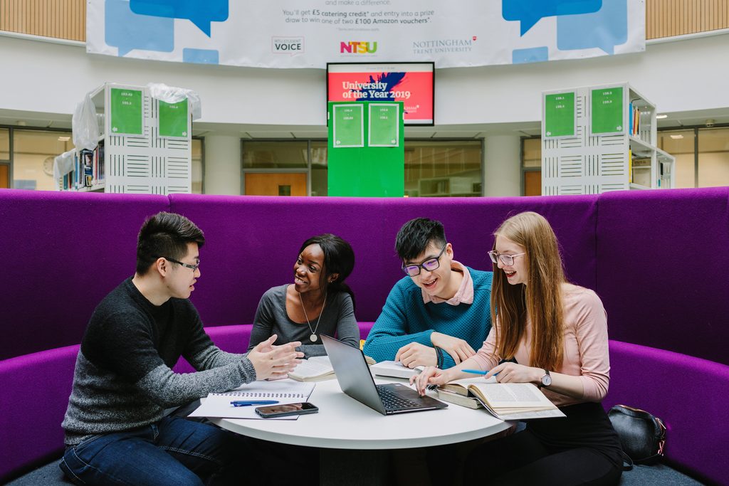 A group of students talking, looking a laptop and studying together