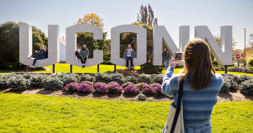 A student in front of the UCONN sign at the university campus