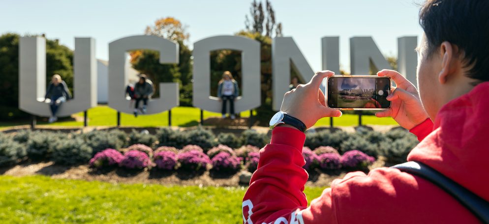 A student taking a picture of his friends in front of the UCONN sign