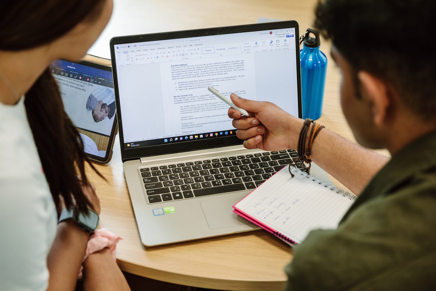 A student pointing at his laptop showing somethinng to another student