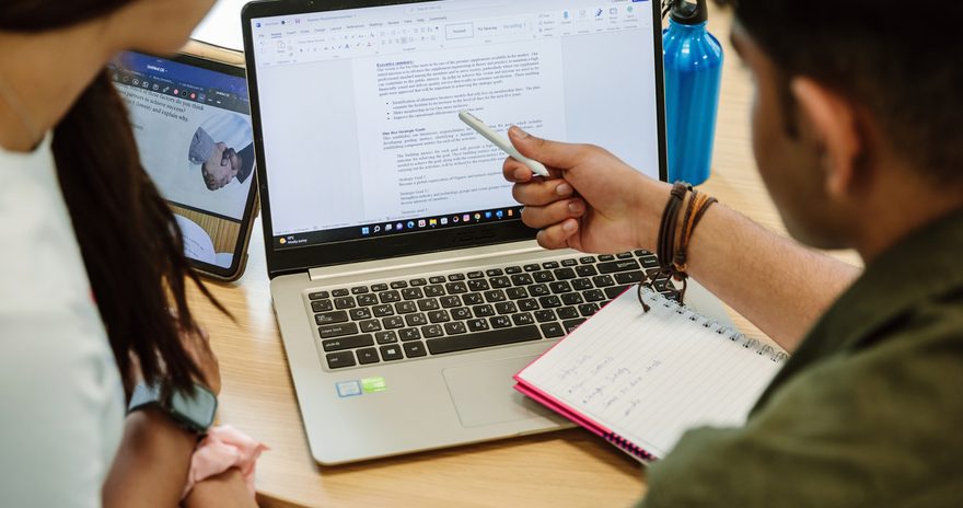 A student pointing at his laptop showing somethinng to another student