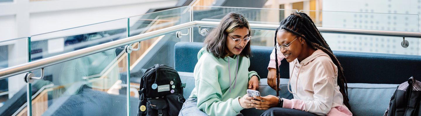 Two students sat down looking at a phone