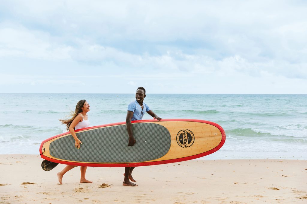 Two students walking on the beach carrying a stand paddle board