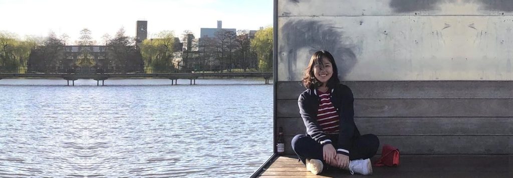 student sitting next at the riverside and smiling to the camera