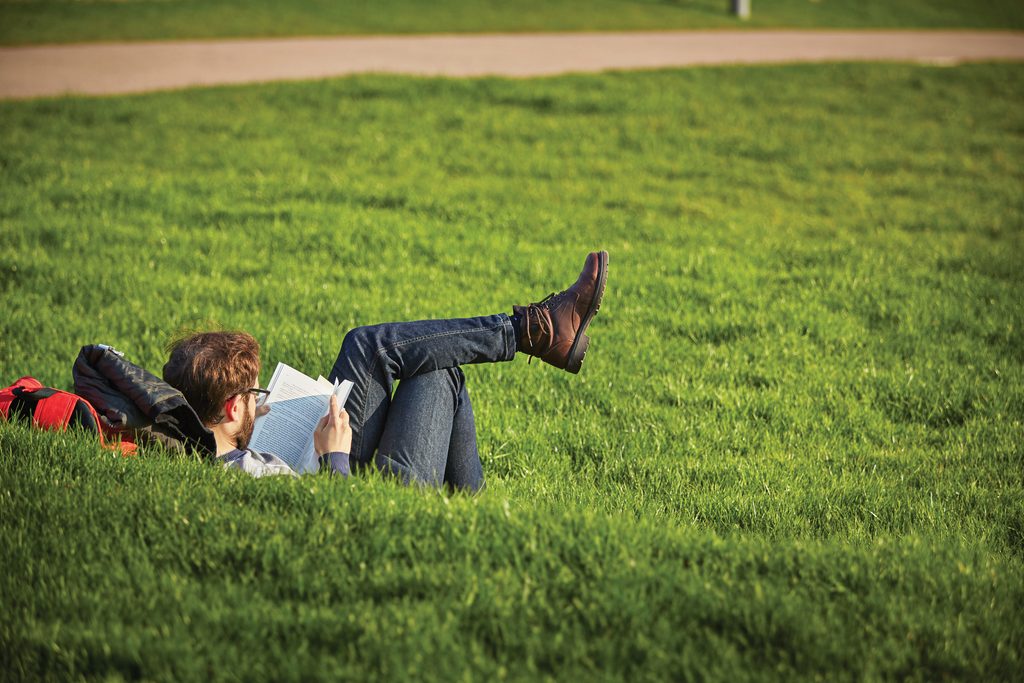 Student reading a book on the grass