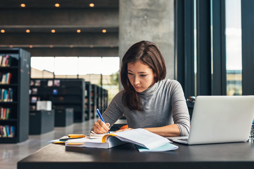 A female student taking notes from a book