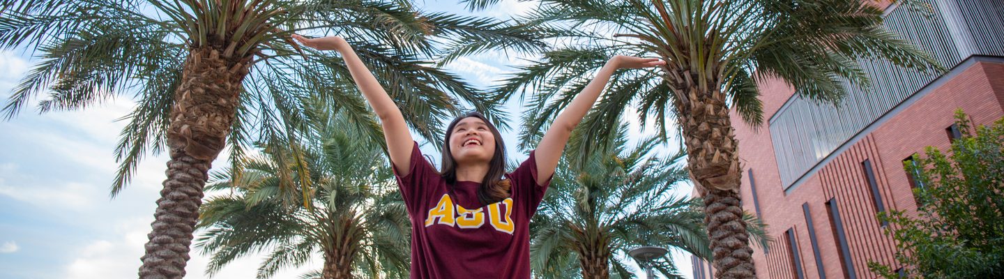 Student raising her arms to the sky and smiling under palm trees