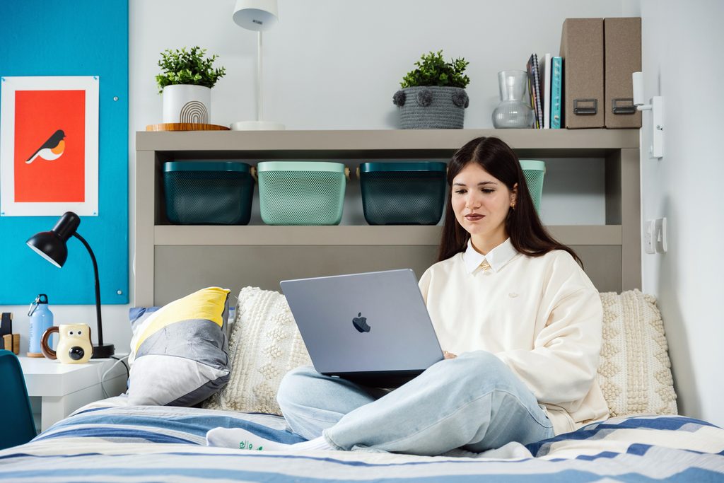 A student sitting on her bed and looking at her laptop