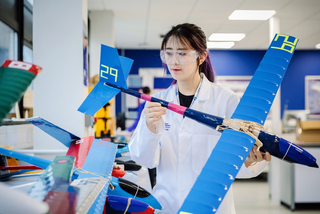 A UNIC student holding a plane model in a lab