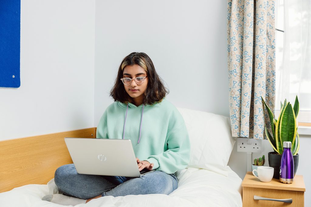 Student sitting on her bed and looking her laptop