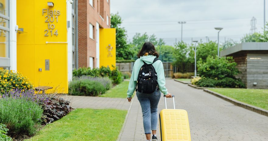 Student walking in the garden with her luggage