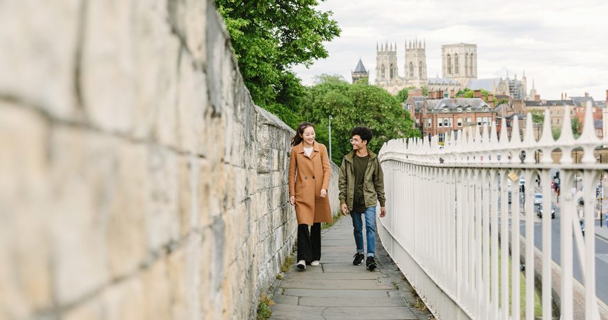 Two students walking in York city with York Minster behind