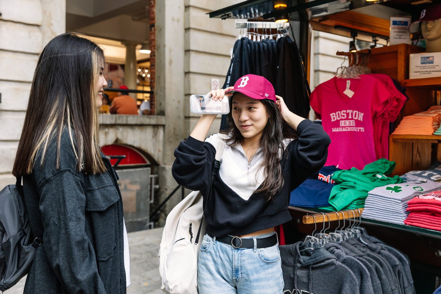 Two students trying clothes in a small store outside