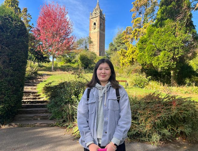 Student standing infront of plants with university in background