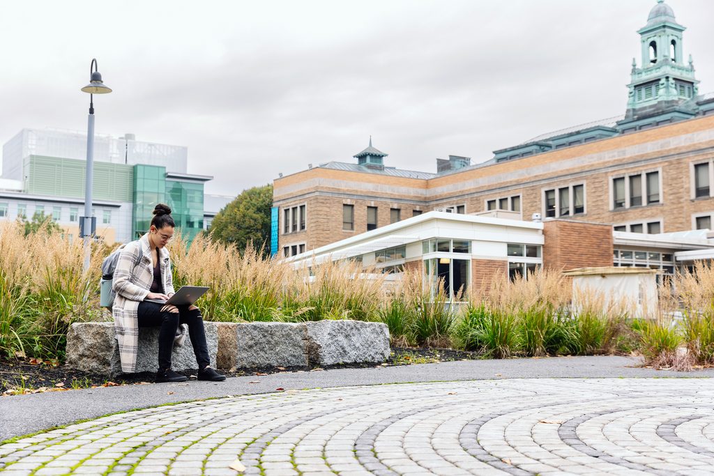 Student sitting and looking at her laptop in the campus yard